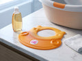 OKbaby hoofdring Flippo Flash oranje op een badkamerplank met babyshampoo - realistische afmetingen